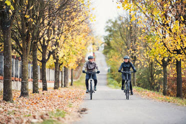 An active senior couple with electrobikes cycling outdoors on a road. - HPIF28750