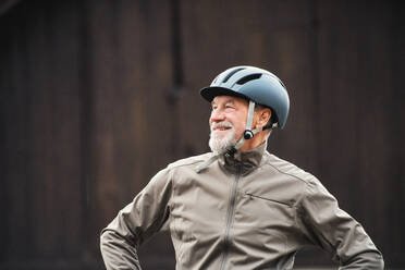 Fröhlicher, aktiver älterer Mann mit Fahrradhelm, der im Freien vor dunklem Hintergrund steht. - HPIF28757