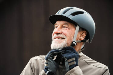 Ein aktiver, fröhlicher älterer Mann steht in der Stadt im Freien und setzt einen Fahrradhelm auf. - HPIF28758