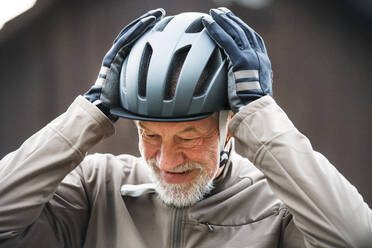 Ein aktiver, fröhlicher älterer Mann steht in der Stadt im Freien und setzt einen Fahrradhelm auf. - HPIF28759