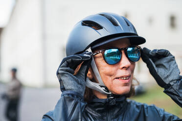 Nahaufnahme einer aktiven älteren Frau mit Fahrradhelm, die im Freien steht und eine Sonnenbrille aufsetzt. - HPIF28766