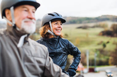 Ein aktives Seniorenpaar mit Helmen und Elektrofahrrädern steht im Freien auf einer Straße in der Natur. Kopierraum. - HPIF28772