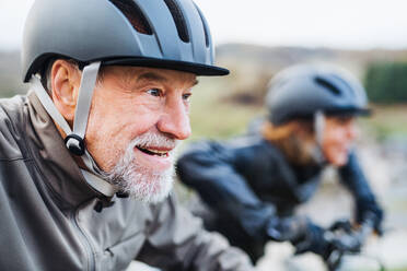 Ein aktives Seniorenpaar fährt mit Helm und Elektrofahrrad auf einer Straße in der Natur. - HPIF28775