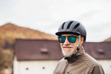 Aktiver älterer Mann mit Fahrradhelm und Sonnenbrille im Freien in der Stadt stehend, Raum kopieren. - HPIF28777