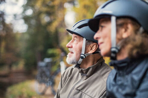 Ein glückliches älteres Paar mit Fahrradhelm, das im Herbst im Freien im Park steht. - HPIF28799