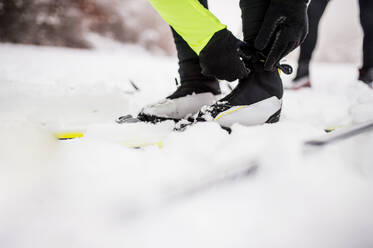 Aktives älteres Paar, das sich zum Skilanglauf bereit macht. Unbekannter Mann und Frau ziehen die Skischuhe an. Winterzeit. - HPIF28810