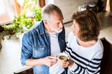 Ein älteres Ehepaar unterhält sich in der Küche, ein alter Mann und eine alte Frau stehen mit einer Tasse Kaffee in der Hand im Haus. - HPIF28815