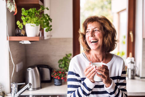 Senior woman in the kitchen. An old woman inside the house, holding a cup of coffee. - HPIF28817