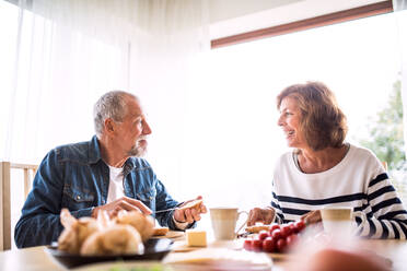 Älteres Ehepaar beim Frühstück zu Hause: Ein alter Mann und eine alte Frau sitzen am Tisch und frühstücken. - HPIF28823