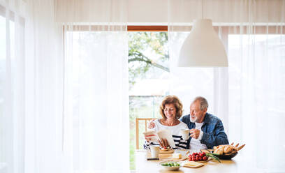 Senior couple eating breakfast at home. An old man and woman sitting at the table, relaxing. - HPIF28833