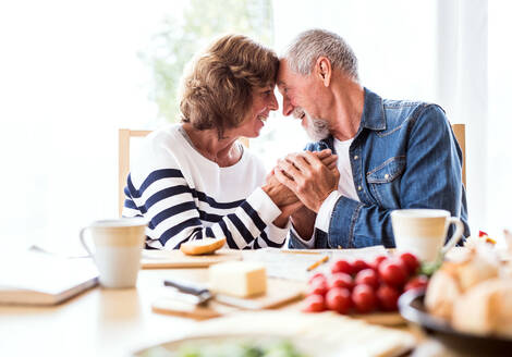 Senior couple eating breakfast at home. An old man and woman sitting at the table, holding hands. - HPIF28836