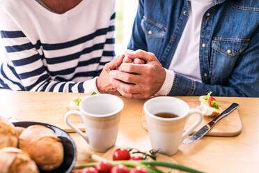 Unbekanntes Seniorenpaar beim Frühstück zu Hause: Ein alter Mann und eine alte Frau sitzen am Tisch und halten sich an den Händen. - HPIF28837