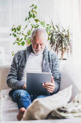 Glücklicher älterer Mann mit Tablet, der sich zu Hause entspannt. - HPIF28847