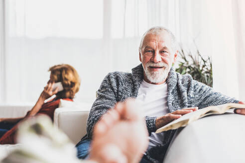 Glückliches älteres Paar mit Smartphone, das sich zu Hause entspannt. Eine Frau telefoniert und ein Mann liest ein Buch. - HPIF28849