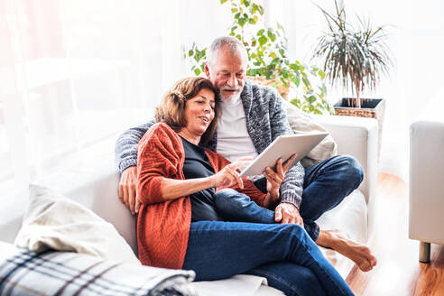 Glückliches Seniorenpaar mit Tablet, das sich zu Hause entspannt. - HPIF28850