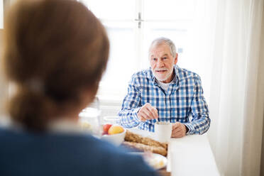 A happy senior couple sitting at the table at home, having breakfast. - HPIF28868