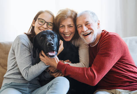 Ein älteres Ehepaar mit einem Mädchen im Teenageralter, das mit seinem Hund zu Hause auf einem Sofa sitzt. - HPIF28906