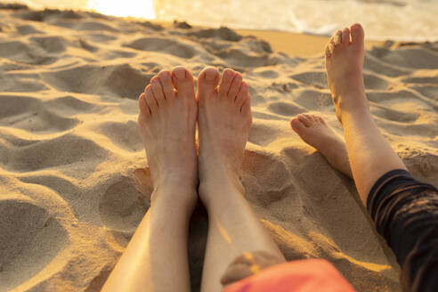 Mutter und Tochter entspannen sich mit nackten Füßen im Sand am Strand - VIVF00941