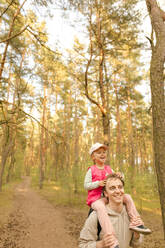 Happy father carrying daughter on shoulder and exploring forest - VIVF00945