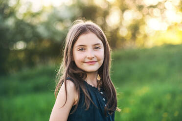 Ein Porträt eines kleinen glücklichen Mädchens, das draußen in der Natur steht. - HPIF28981