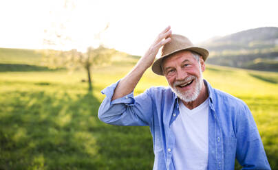 Porträt eines glücklichen älteren Mannes mit Jeanshemd im Frühling in der Natur bei Sonnenuntergang. Kopierraum. - HPIF28982