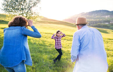 Ein glückliches kleines Mädchen mit ihren älteren Großeltern, die draußen in der Natur Spaß haben. - HPIF28992