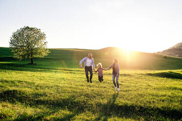 Älteres Paar mit Enkelin, die draußen in der frühlingshaften Natur bei Sonnenuntergang spazieren gehen und springen. - HPIF29004