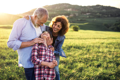 Glückliches älteres Ehepaar mit Enkelin, die draußen in der frühlingshaften Natur stehen und sich bei Sonnenuntergang ansehen. Copy space. - HPIF29005