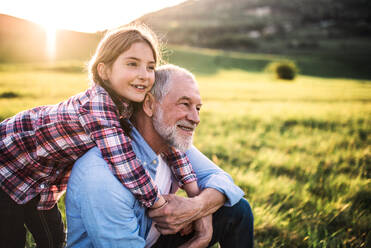 A small girl with grandfather outside in spring nature, relaxing on the grass at sunset. - HPIF29011