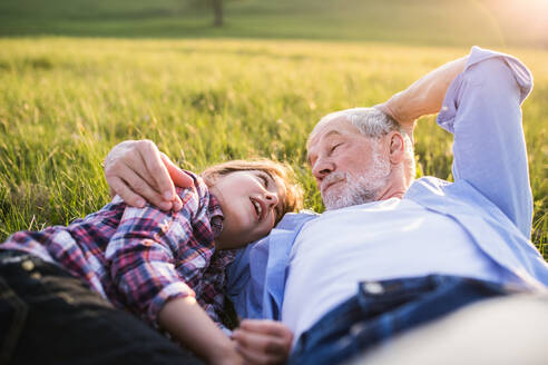 Ein kleines Mädchen mit Großvater draußen in der Natur im Frühling, im Gras liegend, entspannend. - HPIF29014