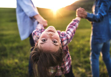 Ein glückliches kleines Mädchen mit ihren unerkennbaren älteren Großeltern, die draußen Spaß haben. Sonnenuntergang im Frühling in der Natur. - HPIF29036