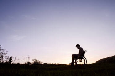 Silhouette eines jungen Mannes im Rollstuhl in der abendlichen Natur, Raum kopieren. - HPIF29044