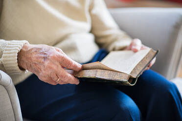 An unrecognizable senior woman sitting on an armchair at home at Christmas time, reading Bible. - HPIF29059
