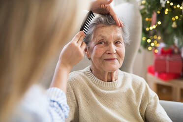 Eine nicht wiederzuerkennende Krankenschwester kämmt die Haare einer älteren Frau, die zur Weihnachtszeit zu Hause auf dem Sofa sitzt. - HPIF29066