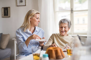 A senior woman in wheelchair with a health visitor sitting at the table at home, eating. - HPIF29088