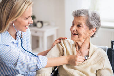 Eine junge Gesundheitsberaterin untersucht eine ältere Frau zu Hause mit einem Stethoskop. - HPIF29101
