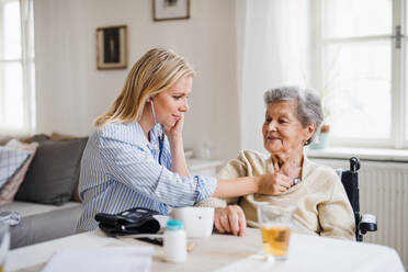 Eine junge Gesundheitsberaterin untersucht eine ältere Frau zu Hause mit einem Stethoskop. - HPIF29102