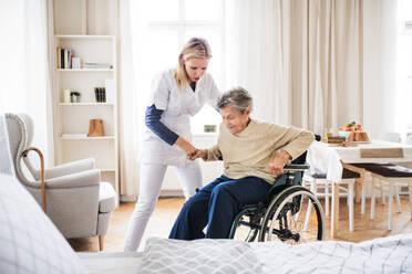 A young health visitor helping a senior woman to stand up from a wheelchair at home. - HPIF29104