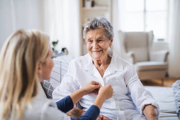 A young health visitor helping a happy sick senior woman sitting on bed at home. - HPIF29125