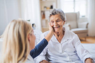 Eine junge Gesundheitsberaterin im Gespräch mit einer glücklichen kranken älteren Frau, die zu Hause im Bett sitzt. - HPIF29126