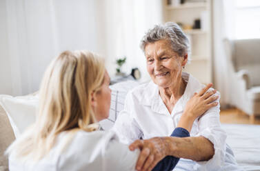 A young health visitor talking to a happy sick senior woman sitting on bed at home. - HPIF29127