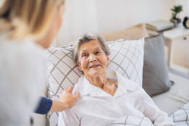 A young health visitor talking to a happy sick senior woman lying in bed at home. - HPIF29130