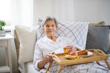 Eine ältere, kranke Seniorin mit Essen auf einem Holztablett, die zu Hause im Bett liegt. - HPIF29149