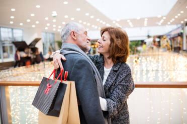 Happy senior couple with paper bags in shopping center looking at each other, hugging. - HPIF29157