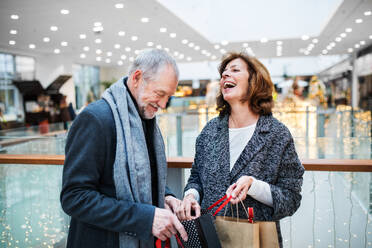 Ein älteres Ehepaar mit Papiertüten im Einkaufszentrum zur Weihnachtszeit, lachend. - HPIF29159