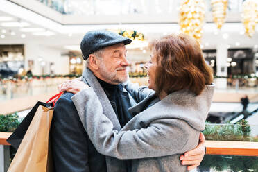 Glückliches älteres Ehepaar mit Papiertüten in einem Einkaufszentrum, die sich gegenseitig ansehen und umarmen. - HPIF29167