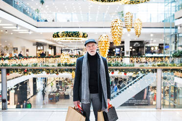 A portrait of bored and tired senior man with paper bags standing in shopping centre at Christmas time. - HPIF29168