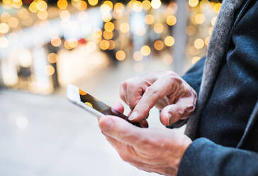 Unbekannter älterer Mann mit Smartphone in einem Einkaufszentrum zur Weihnachtszeit, Textnachrichten schreiben, Nahaufnahme. - HPIF29174