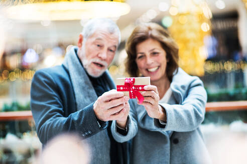 Ein Porträt eines älteren Paares, das ein eingepacktes Geschenk in einem Einkaufszentrum zur Weihnachtszeit vor sich hält. - HPIF29178