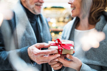 Ein unerkanntes älteres Ehepaar hält ein eingepacktes Geschenk in einem Einkaufszentrum zur Weihnachtszeit vor sich. - HPIF29179